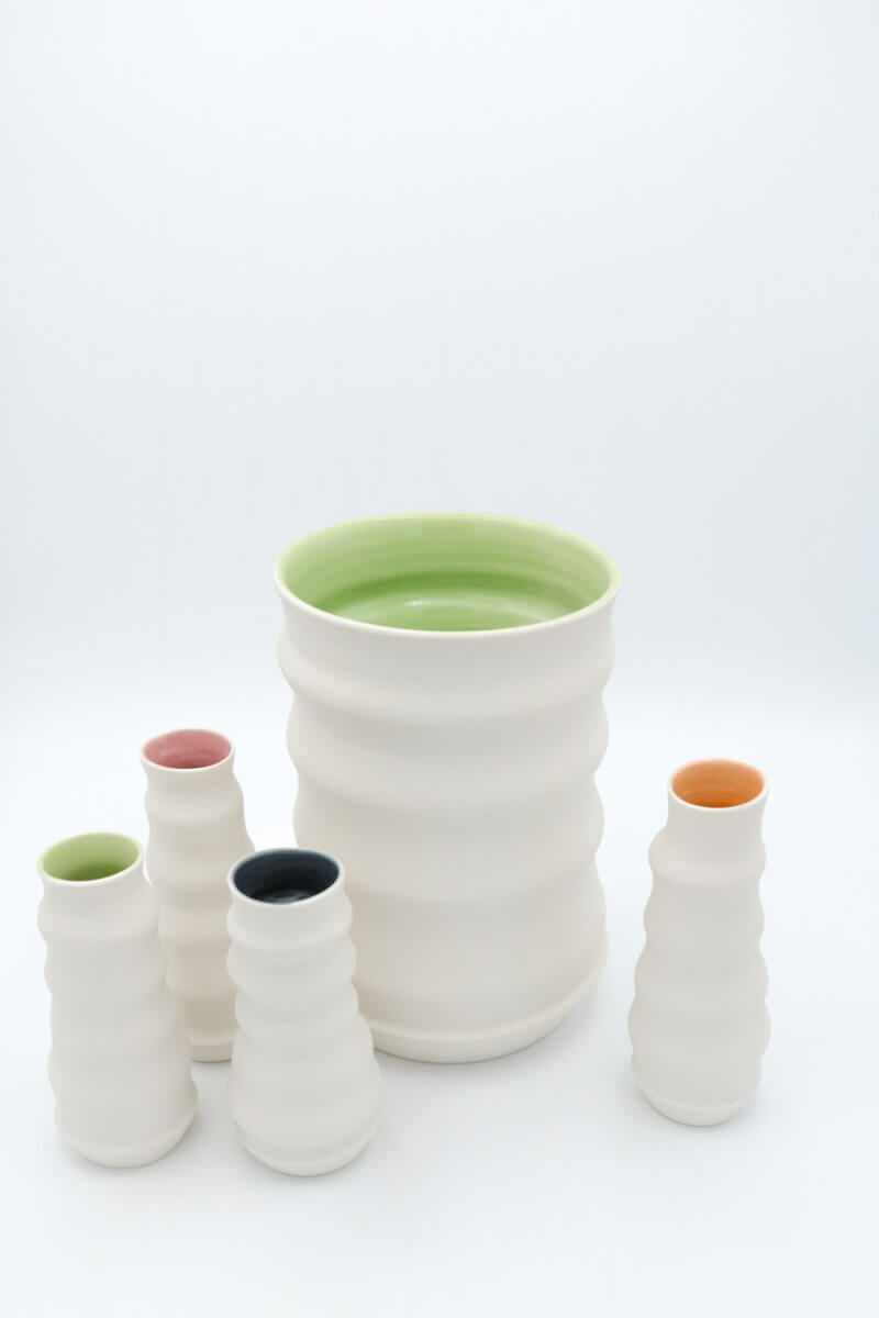 Vasen von Sandra Nitz außen weiß und innen bunt eine große grüne Vase steht in der Mitte